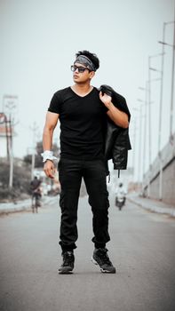 Fashionable man in black outfit posing confidently on an urban street.