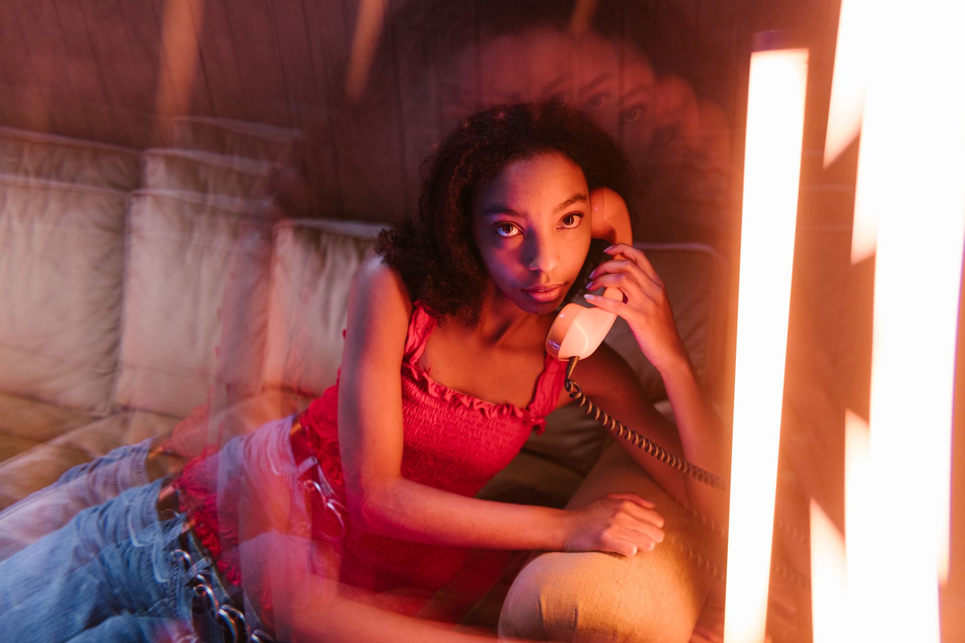 A fashionable woman in a pink top relaxes on a couch while holding a vintage telephone indoors.