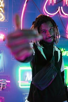 A young man with dreadlocks poses confidently under vibrant neon lights in a nightclub.
