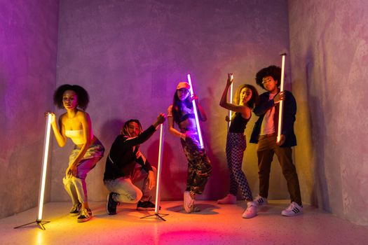 Dynamic group of young adults posing with neon lights in a colorful, artistic setting.