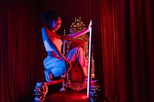 Striking portrait of a woman poised on a gold throne, illuminated by vibrant stage lighting.