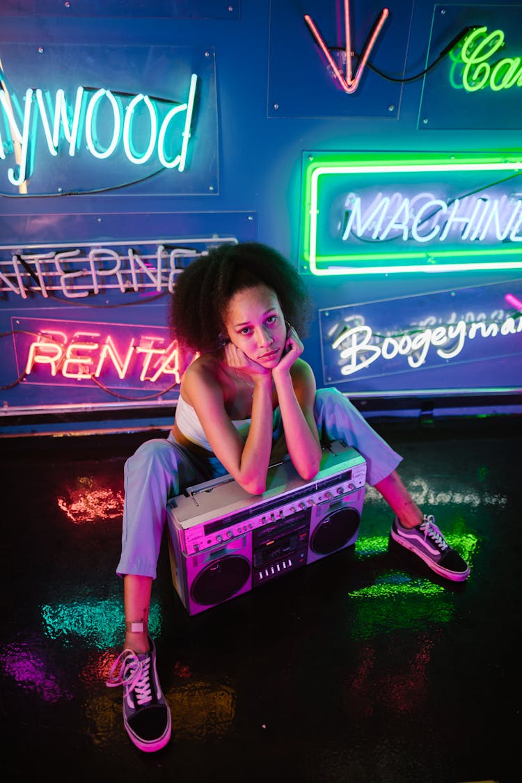 A Woman Sitting On The Floor Leaning On A Boombox