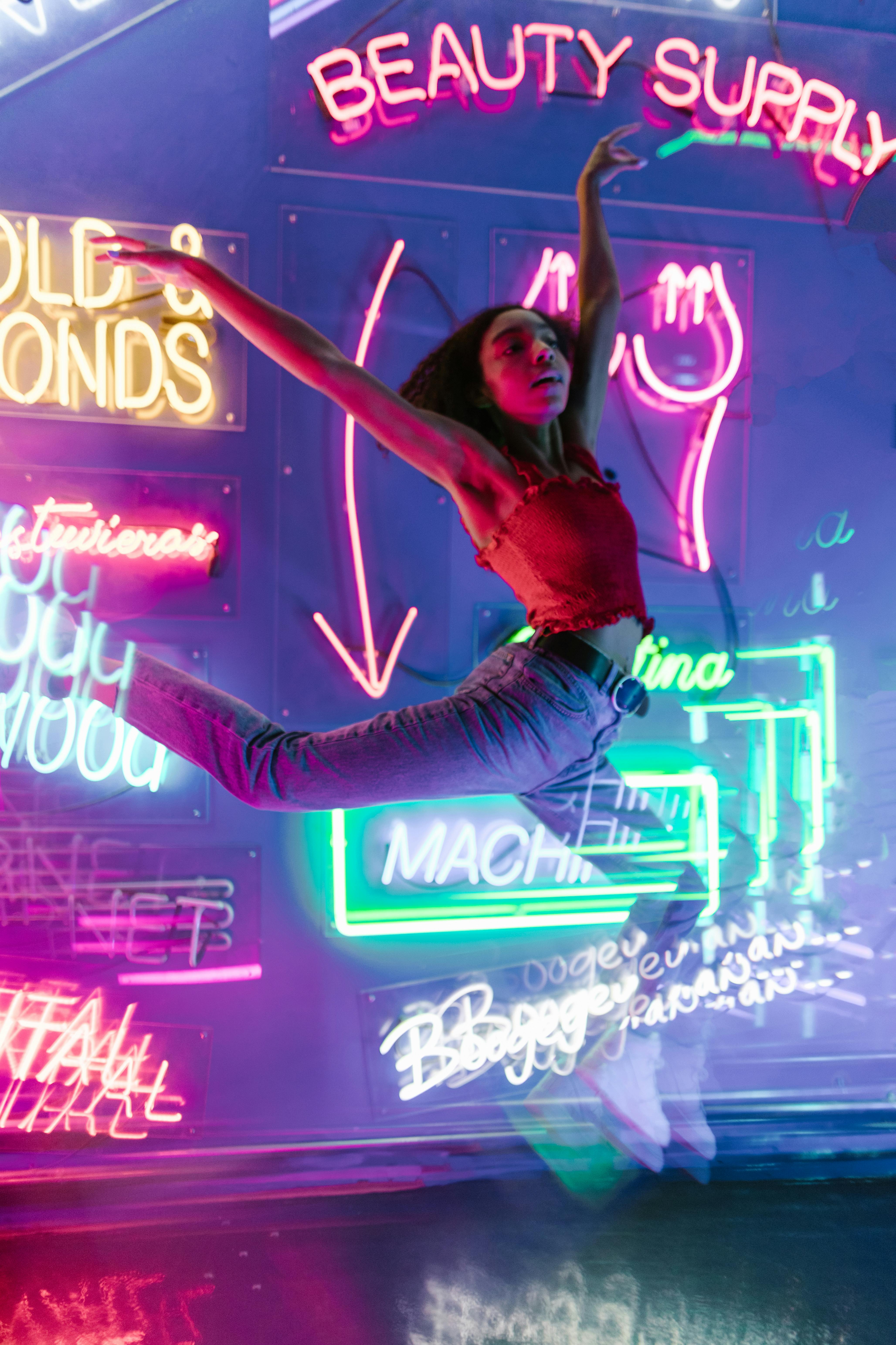 a woman midair in front of a wall with neon signs