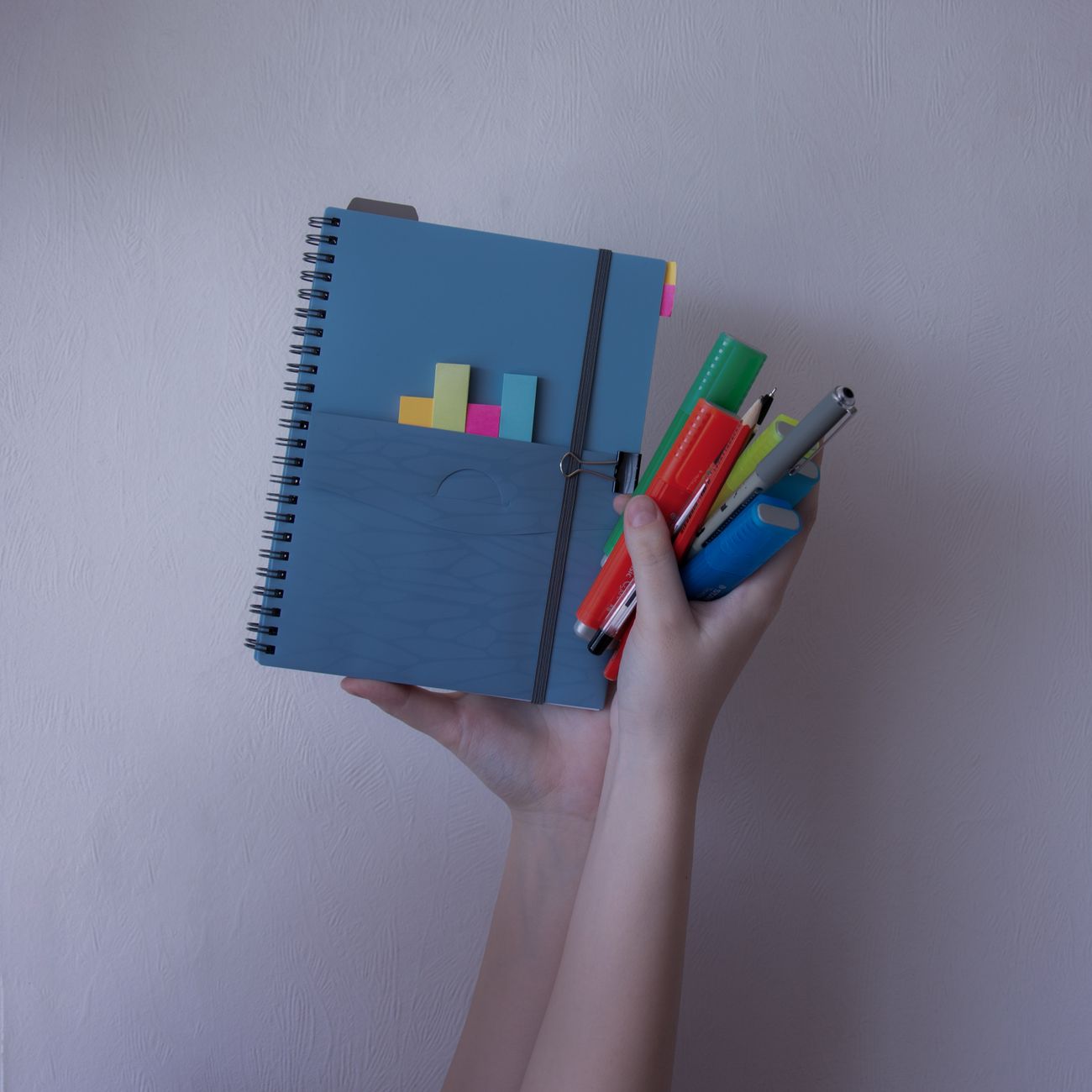 A person holding a notebook with colorful pens and sticky notes