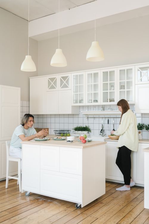 Free A couple enjoying time in a bright, modern kitchen with wooden flooring. Stock Photo