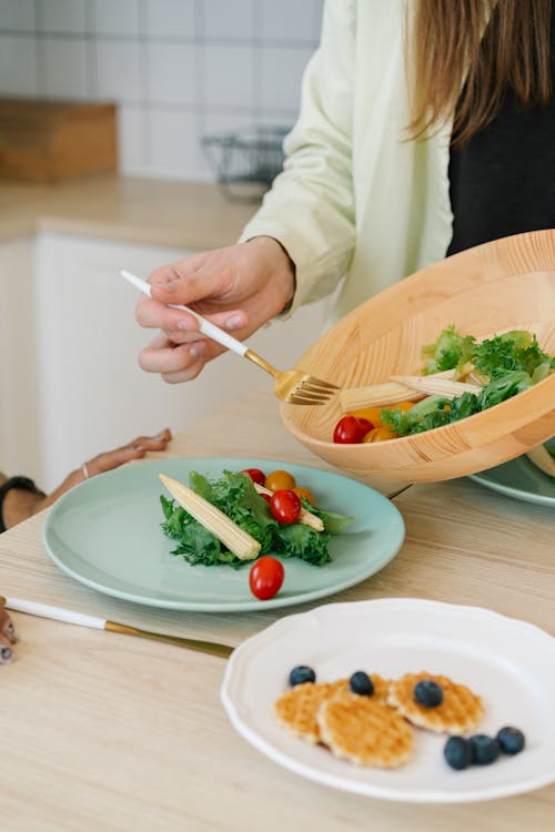 Free Person Holding Fork Transferring Vegetables From Bowl to Plate Stock Photo