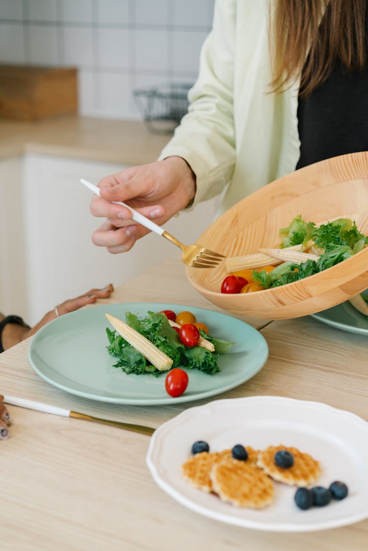 Person Holding Fork Transferring Vegetables From Bowl To Plate