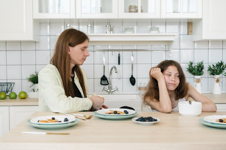 A Young Girl Frowning While Sitting Beside His Father