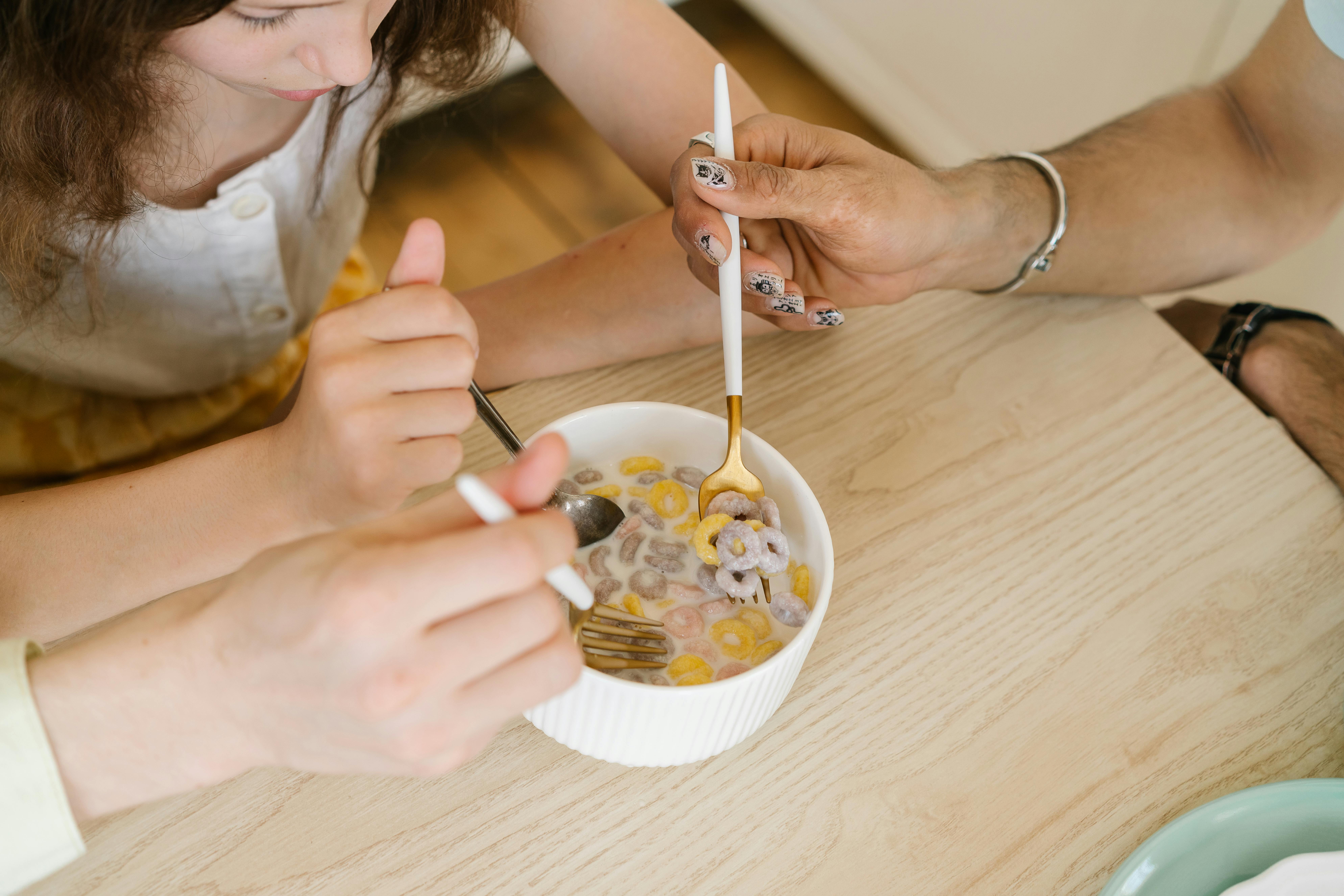 Two people enjoying breakfast with a colorful cereal bowl on a wooden table.