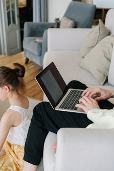 A parent typing on a laptop with a child sitting nearby, enjoying a cozy home setting.