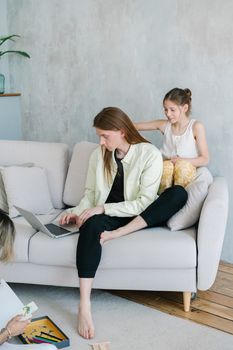 Father using laptop while daughter plays at home, creating a cozy family moment on the sofa.