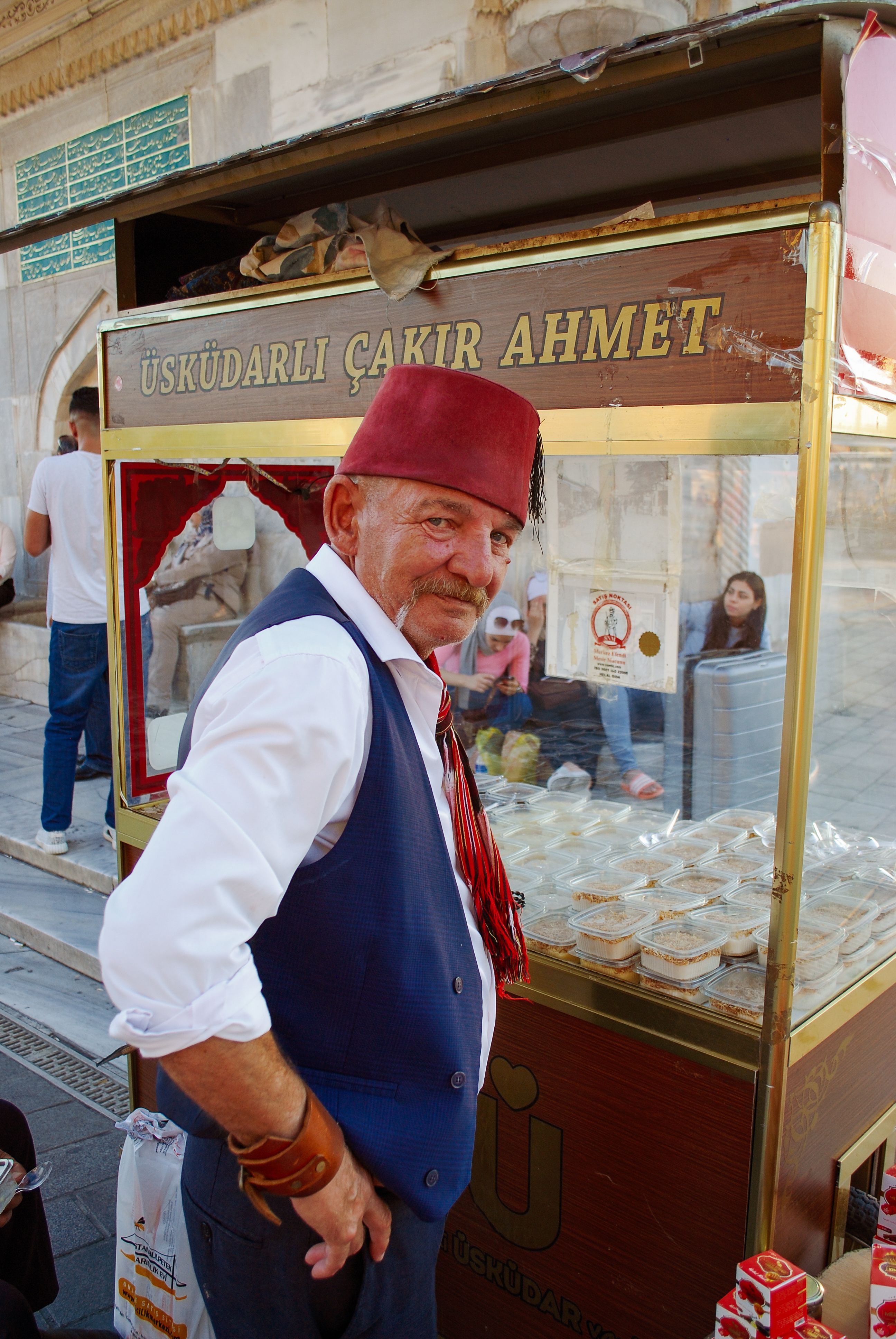 Elderly man in traditional attire selling food on the streets of Istanbul at a wooden cart.