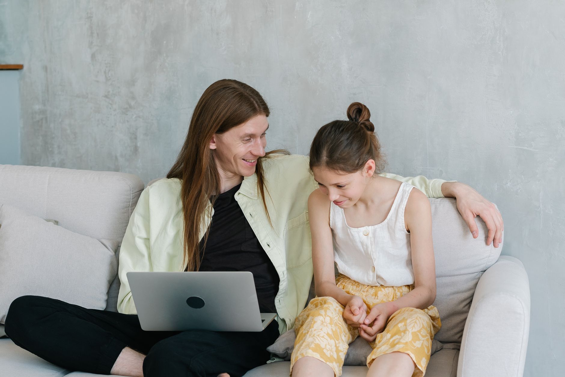 A father and daughter sitting together on a couch using a laptop, sharing a joyful moment.