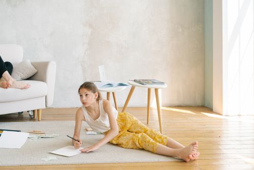 Free A young girl engaged in drawing on the wooden floor in a cozy, sunlit room. Stock Photo