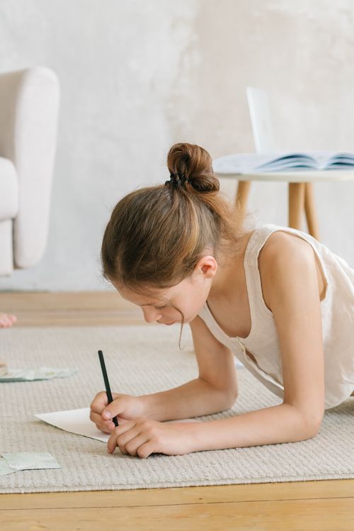 Free Child engrossed in drawing on carpet at home, creating an artistic scene in a cozy living room. Stock Photo