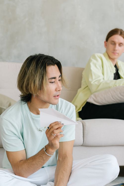 Free Two young adults in a relaxed home environment holding a paper plane. Stock Photo