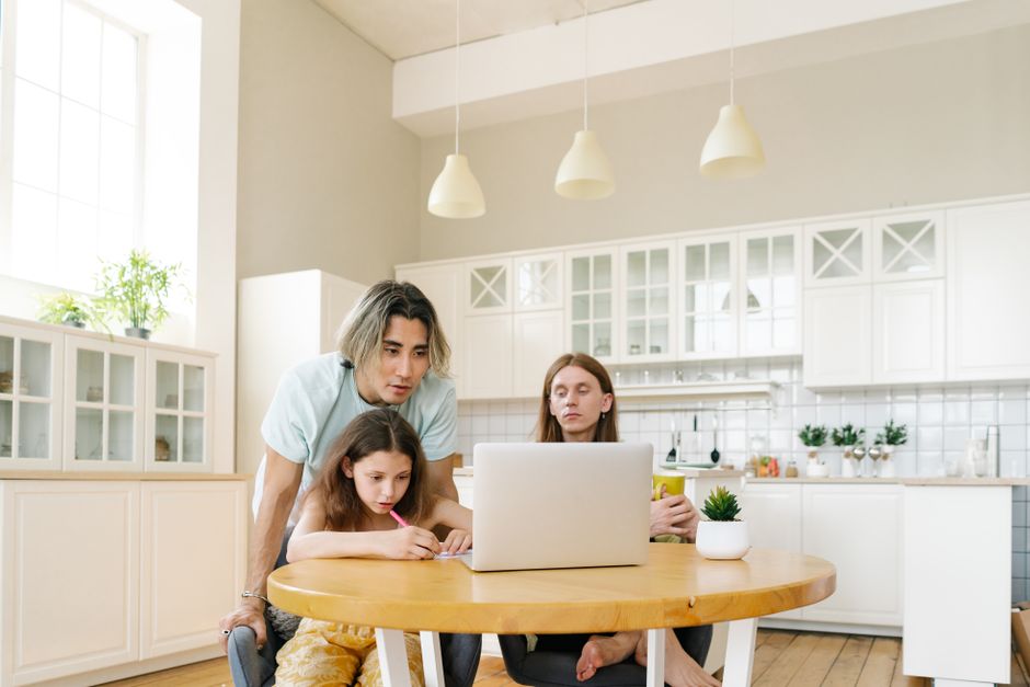 A family engaged in home learning around a laptop in a bright, modern kitchen, fostering education.