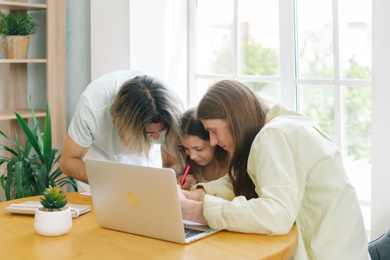 Two adults helping a child with work at a table