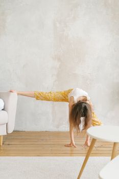 Child energetically stretching indoors, using sofa for support, in a bright home environment.