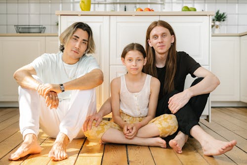 A Same Sex Couple Sitting on a Wooden Floor with their Daughter