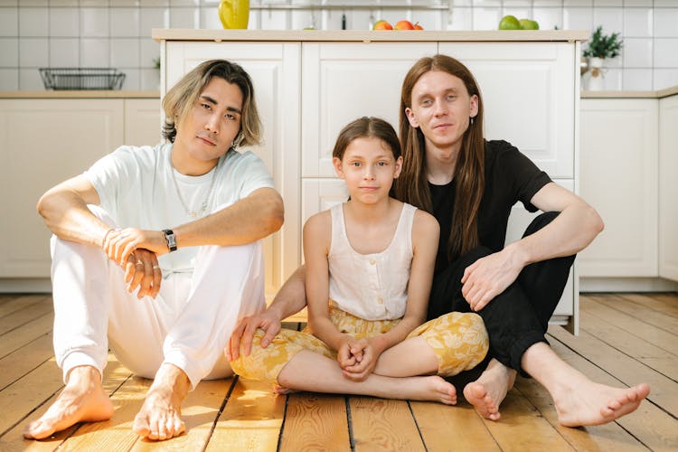 A Same Sex Couple Sitting On A Wooden Floor With Their Daughter