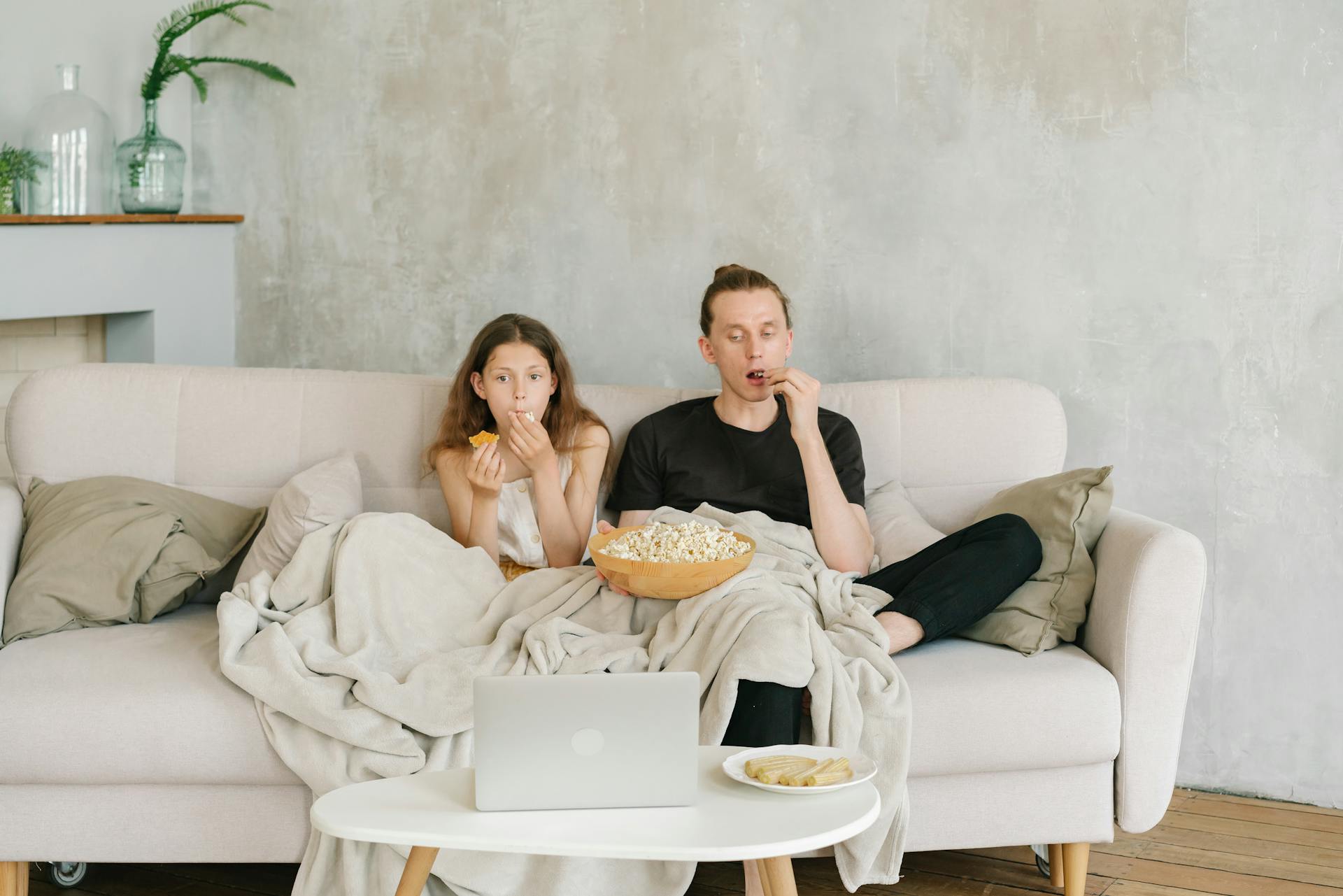 A Father and Daughter Eating Popcorn while Watching on Laptop