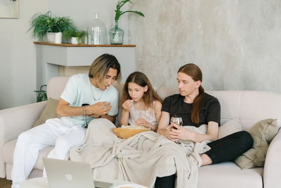 A family watching a film with popcorn on the couch — photo by Mikhail Nilov on Pexels