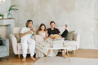 Three young friends enjoying a movie night on the sofa with popcorn and drinks.