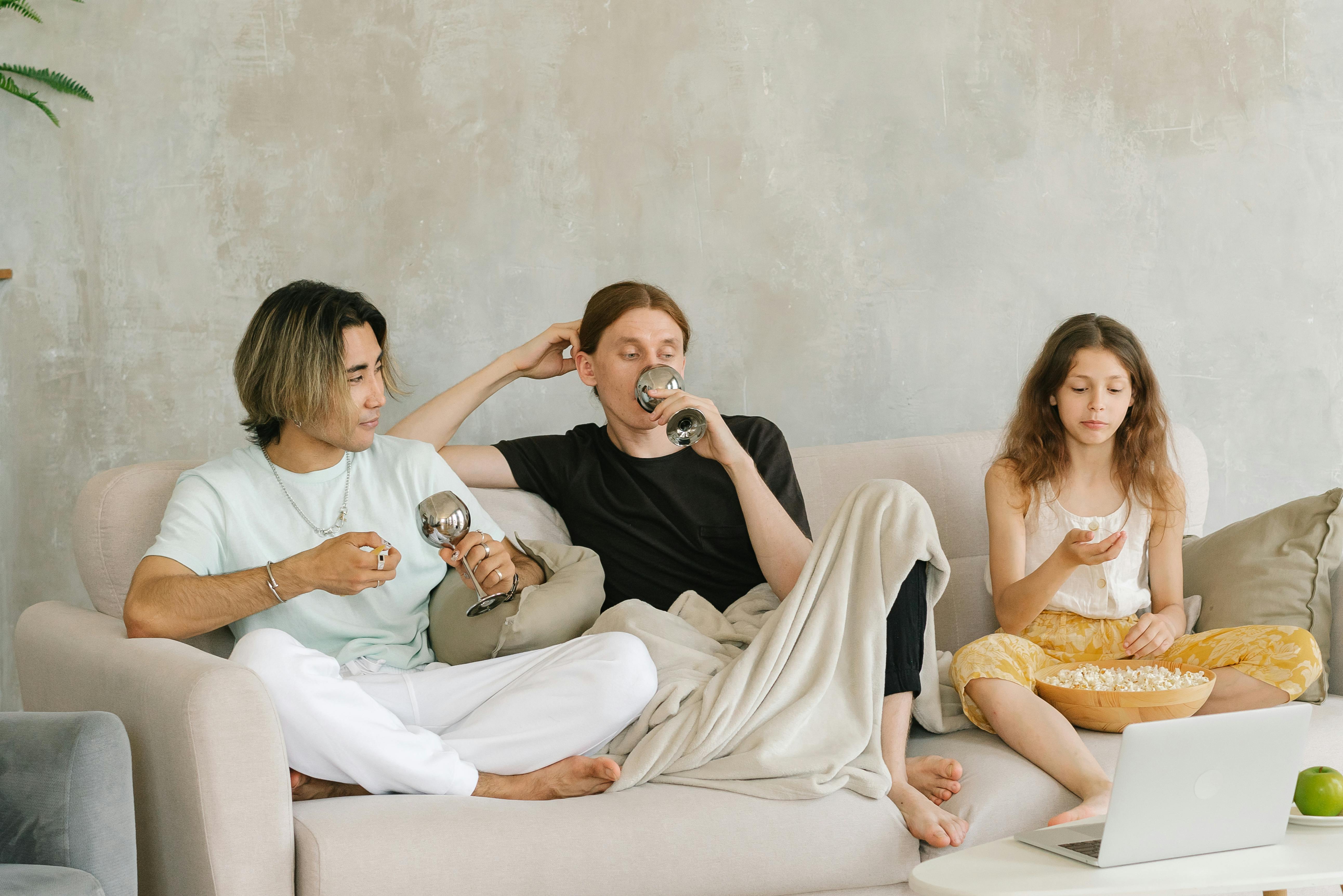 A family relaxing on a couch, enjoying popcorn and wine while watching a movie.