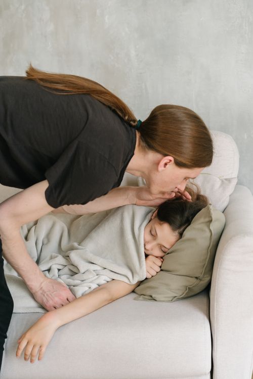 Free Father lovingly kisses his sleeping daughter on the sofa, wrapped in a blanket. Stock Photo