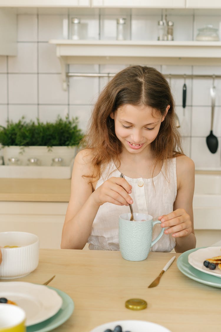 Teenage Girl Holding A Spoon And Mug On A Wood Table