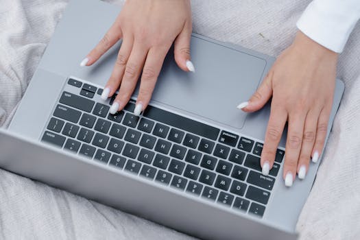 Close-up of manicured hands typing on a laptop keyboard, showcasing modern technology use.
