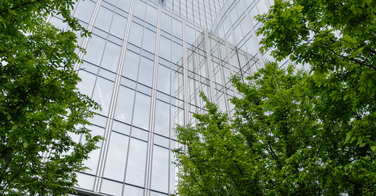 Striking low-angle view of a modern glass skyscraper surrounded by vibrant green trees.