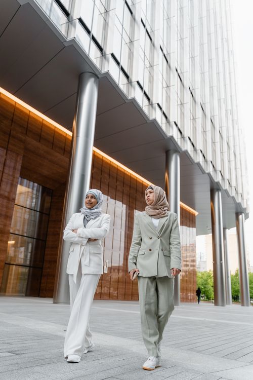 Free Two women in hijabs and suits walk confidently outside a modern office building. Stock Photo