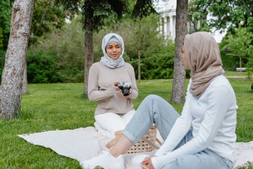 Free Two women in hijabs having a peaceful outdoor picnic, engaging in conversation in a green park setting. Stock Photo