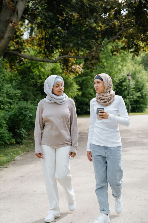 Free Two women in hijabs enjoy a walk in a green park, engaging in conversation. Stock Photo