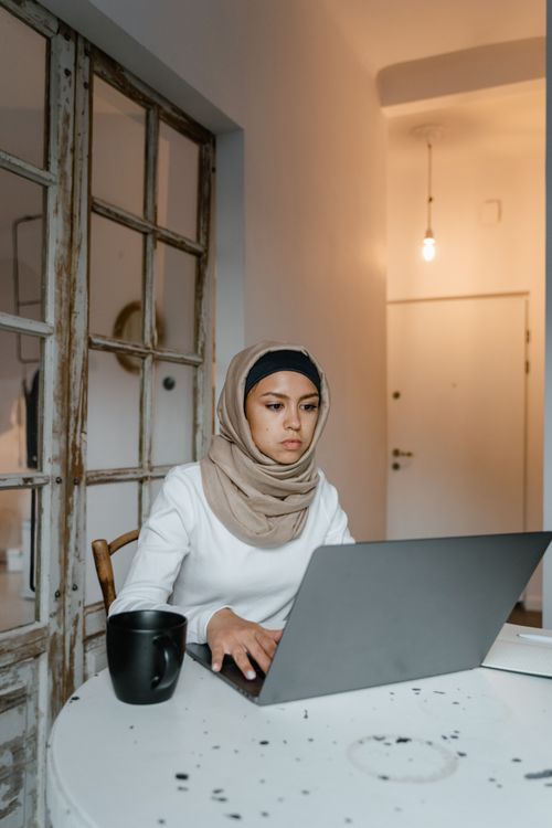Free Woman in hijab working on a laptop at a cozy indoor workspace. Stock Photo