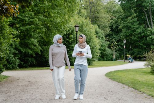 Free Two women in hijabs walking and conversing in a lush green park on a sunny day. Stock Photo