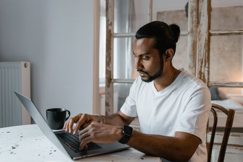 Free A bearded man is focused while typing on his laptop at home, seated at a desk. Stock Photo