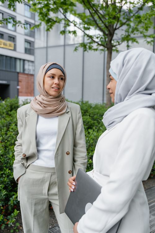 Free Two professional women wearing hijabs engage in a conversation outside an office building. Stock Photo