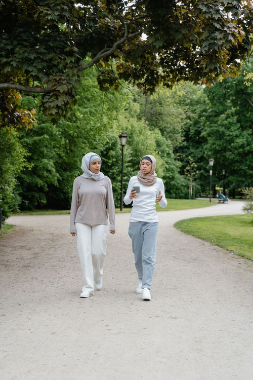 Free Two women wearing hijabs walk and converse in a lush green park setting. Stock Photo