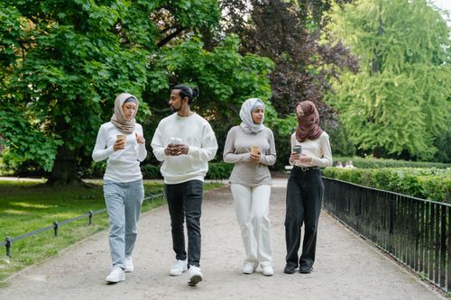 Free Group of young adults walking together with coffee in a scenic park setting during the day. Stock Photo