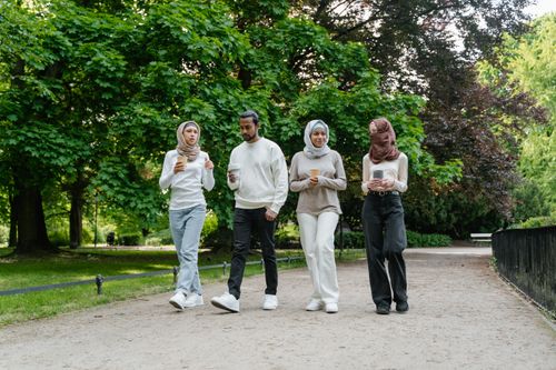 Free Group of diverse friends walking in a park, holding coffee cups and enjoying a sunny day outdoors. Stock Photo