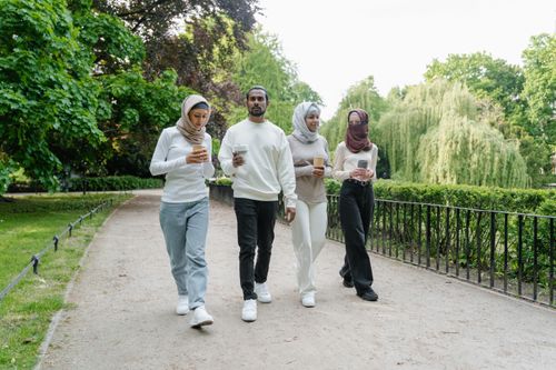 Free Group of friends in hijabs and casual wear walking with drinks in a lush green park setting. Stock Photo