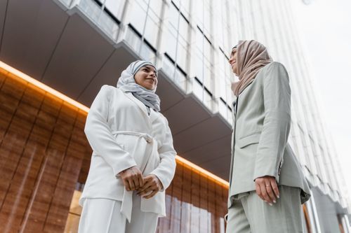 Free Two women in hijabs and business attire conversing outside a modern building. Stock Photo