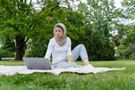 A Woman Holding a Paper Cup and Using a Laptop