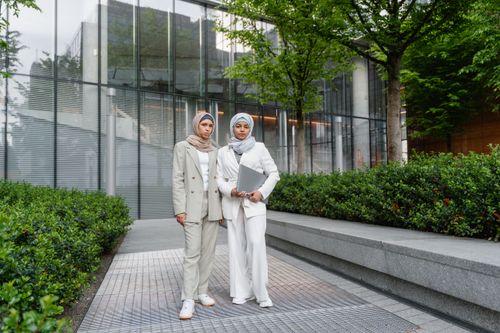 Free Two Muslim women in business attire, holding a laptop, outdoors in a corporate setting. Stock Photo