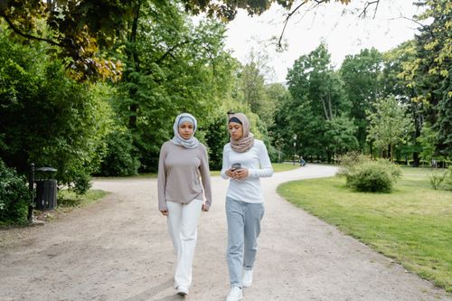 Free Two women in hijabs enjoying a walk and conversation in a lush green park. Stock Photo