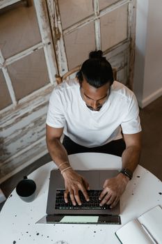 Man in white shirt working on a laptop in a cozy indoor space, top view.