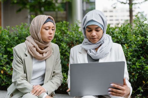 Free Two women in hijabs working together on a laptop outside in a green space. Stock Photo